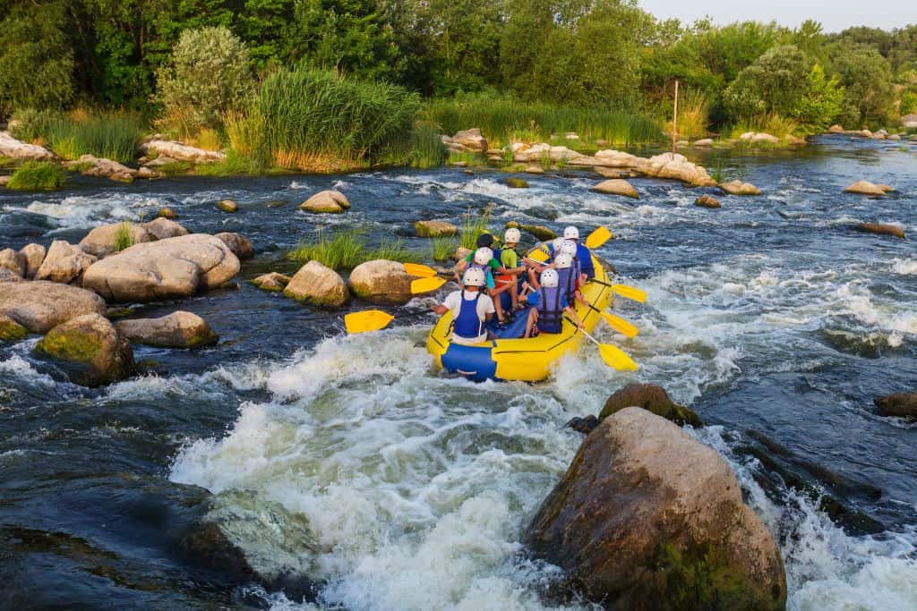 Yellow raft floating down a river with 8 passengers wearing white helmets and blue life jackets