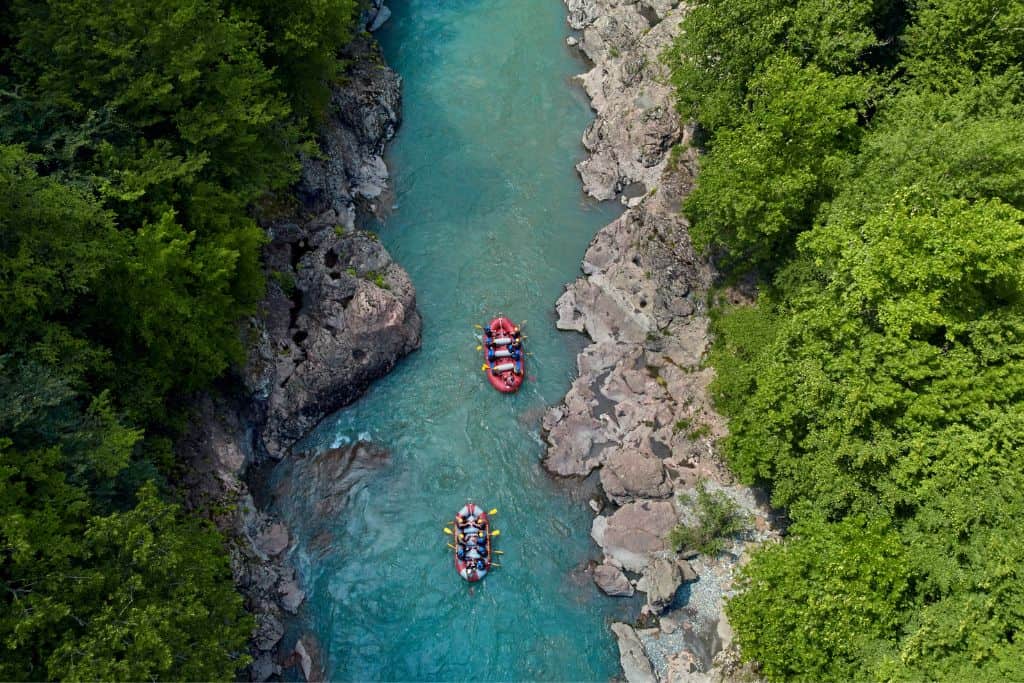 Two red rafts floating down a narrow channel with rocks and trees on either side