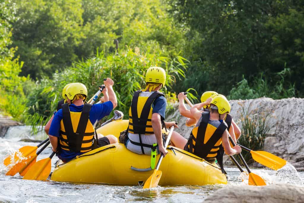 Group of rafters wearing yellow helmets, life jackets, and using yellow paddles on a yellow raft