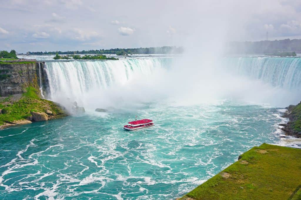Red boat driving near a giant waterfall