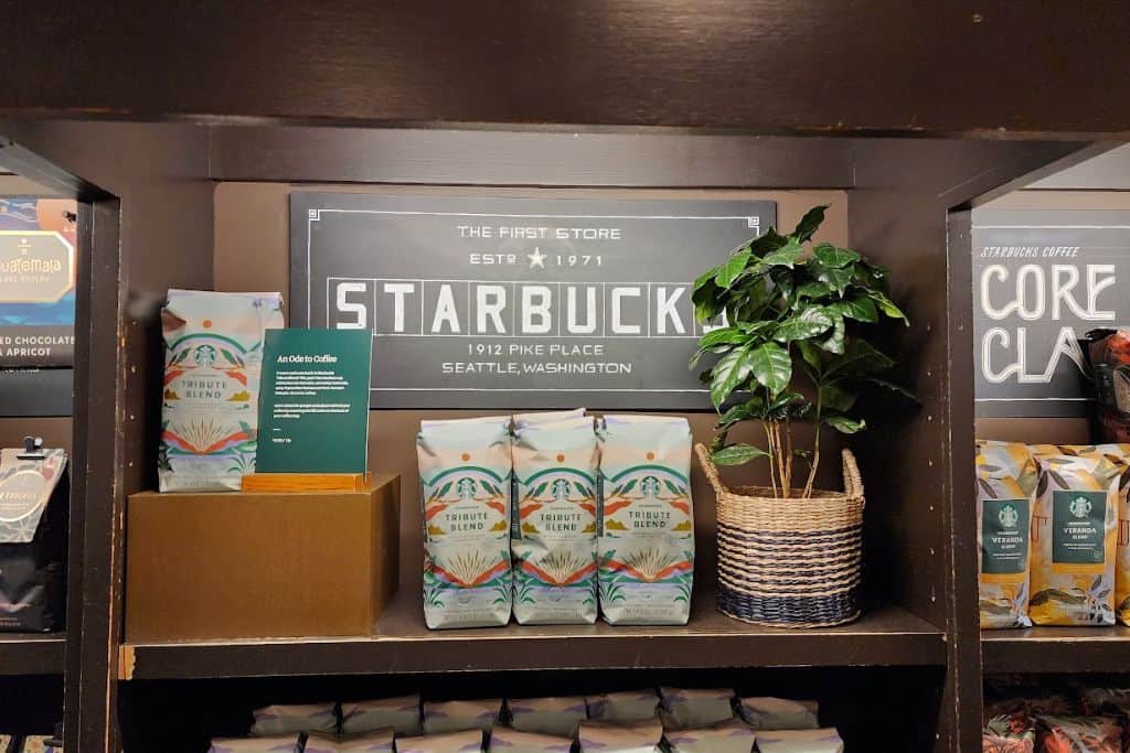 Bags of coffee and a small fake plant under a "Starbucks" sign on a shelf