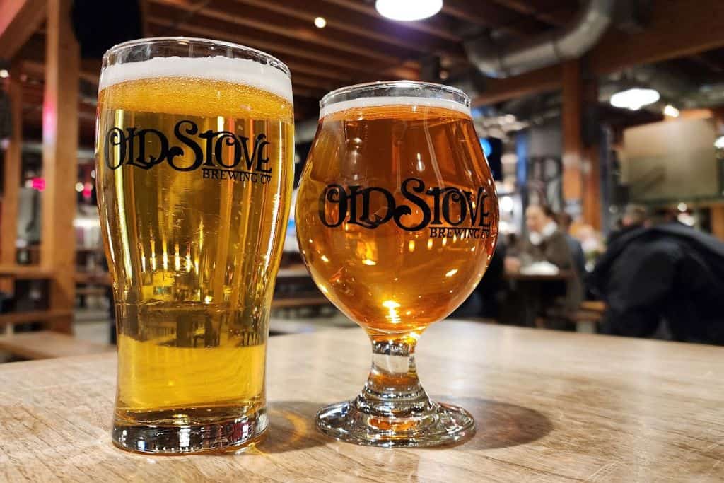 Two beer filled glasses on a table with "Old Stove Brewing" written on them