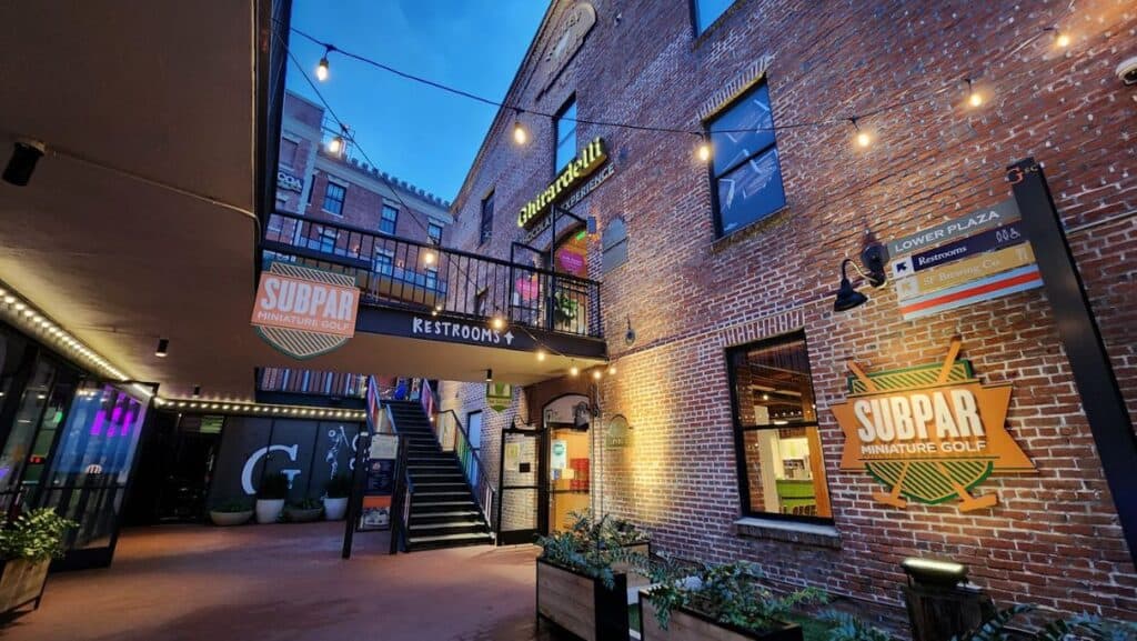 Brick building with black stair case and "Subpar Miniature Golf" sign