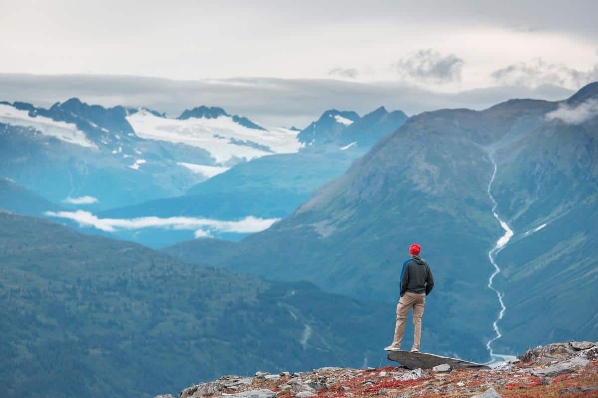 Person standing on a rock ledge overlooking mountains and glaciers