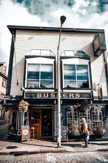Green and white square building on a cobblestone street with the sign "Buskers" on the front