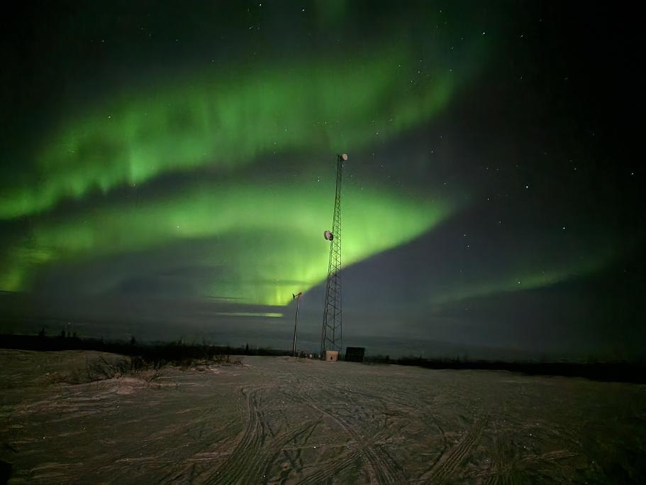 Green northern lights over a snowy road with a metal tower