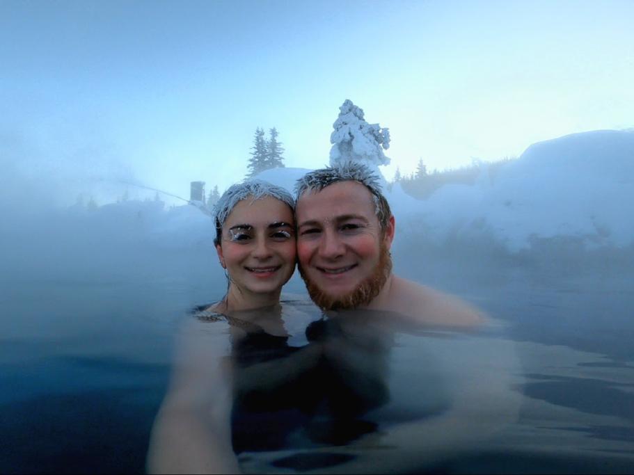 A man and a woman in a hot spring surrounded by snow-covered trees