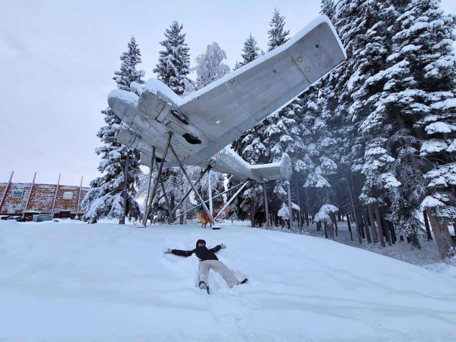 A man making a snow angel under an airplane statue
