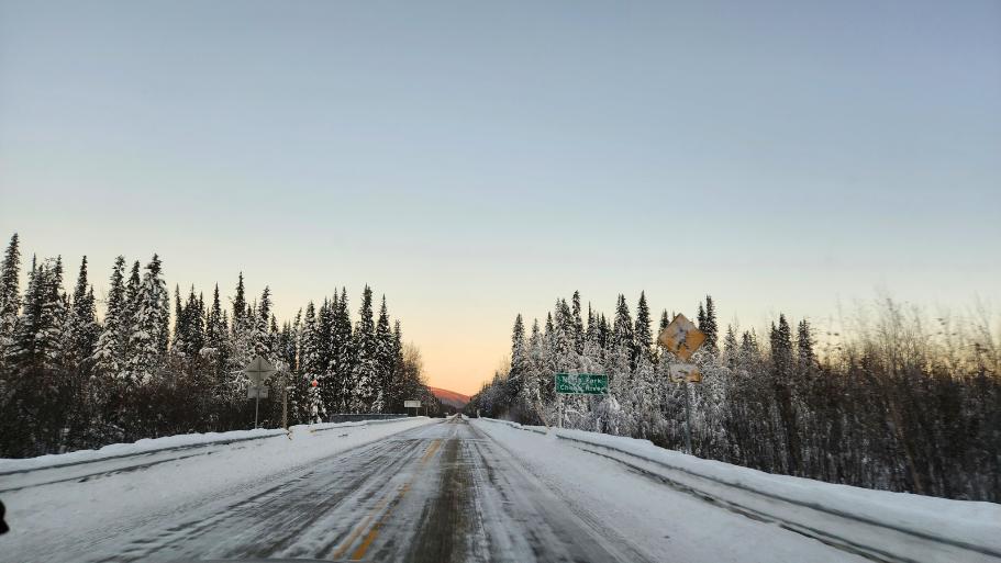 Snowy road with pine trees and a golden sunset