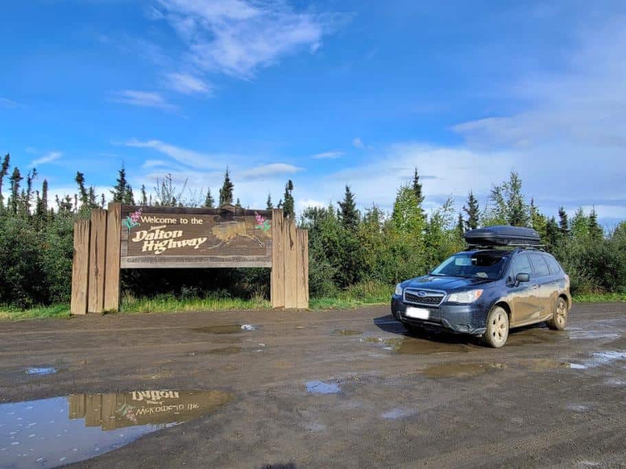 Subaru Forester car parked next to the "Welcome to the Dalton Highway" sign on a muddy road