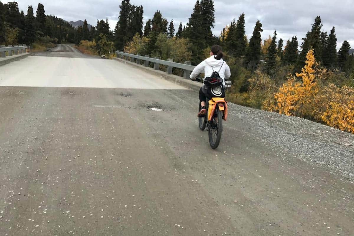 Girl on yellow bike riding on a dirt and gravel road in the woods