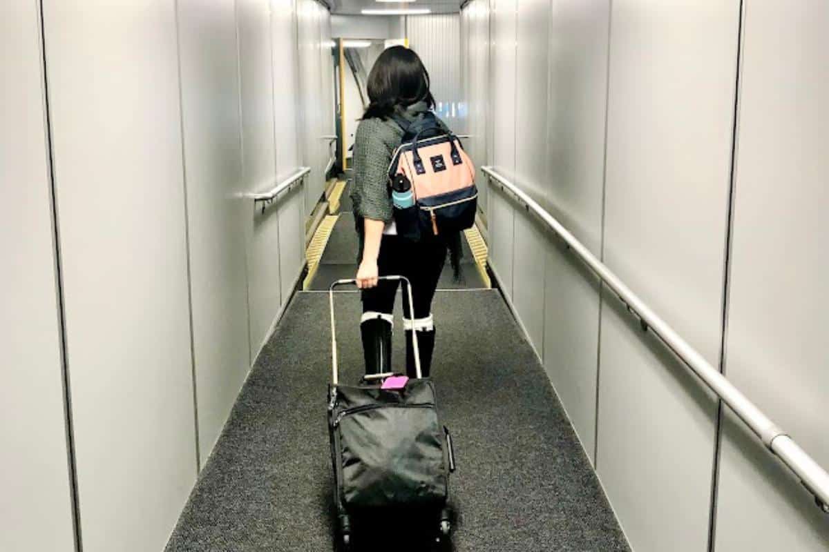 Girl with a pink backpack and black suitcase walking down an airplane jetway