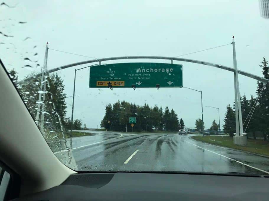 Car interior with rainy windshield and blurry green "Anchorage" sign