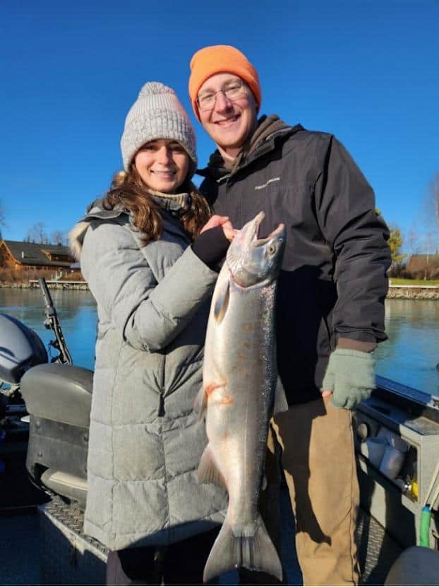 Man and woman dressed in winter gear holding a large fish on a small power boat