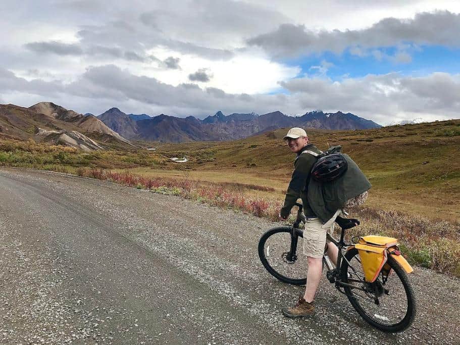 A man sitting on a bicycle with the Denali mountains in the background