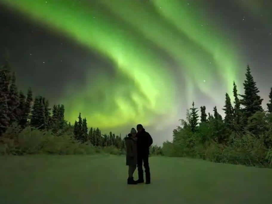 The silhouette of a man and woman standing under green northern lights