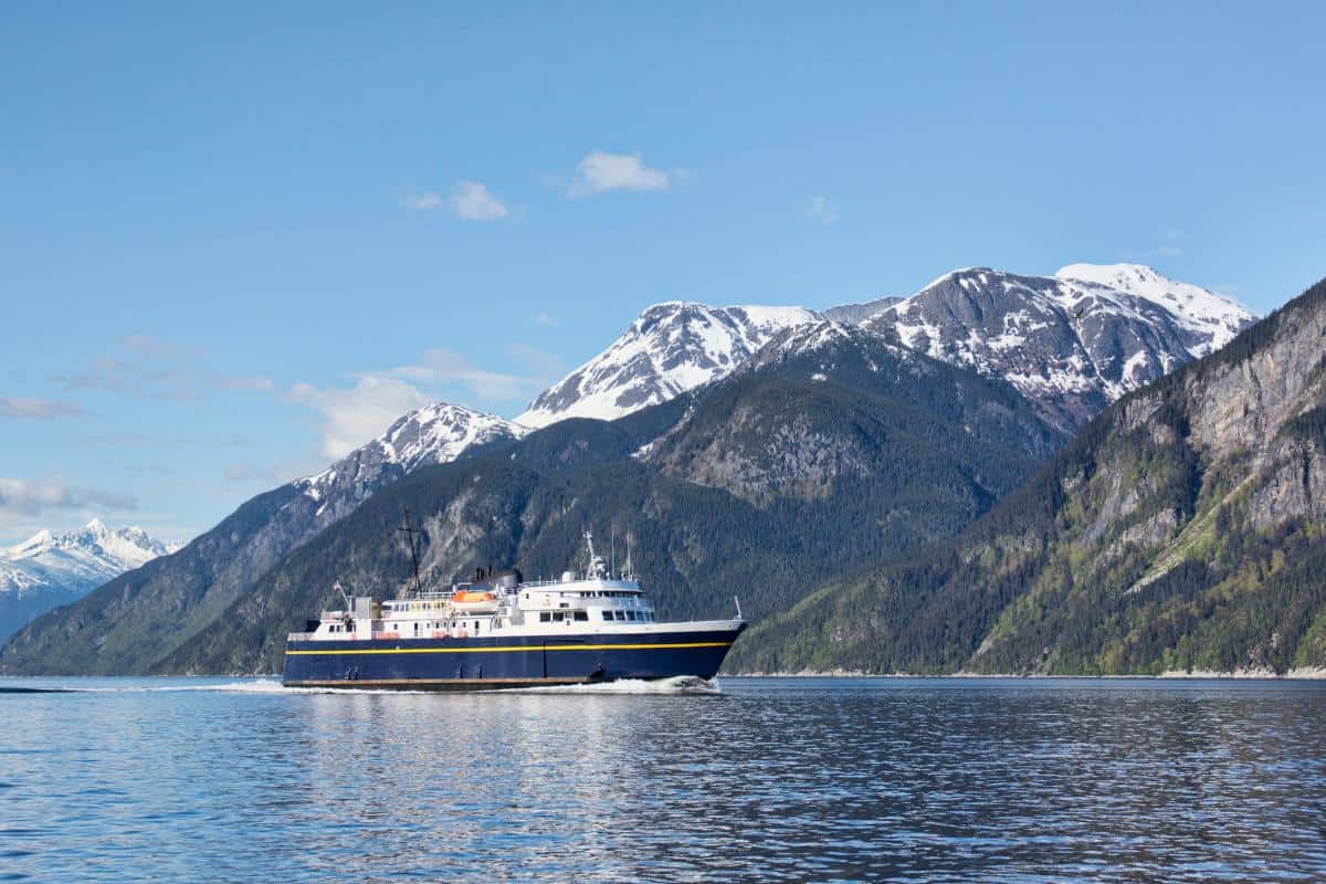 Large blue and white ferry cruising alongside snowy mountains
