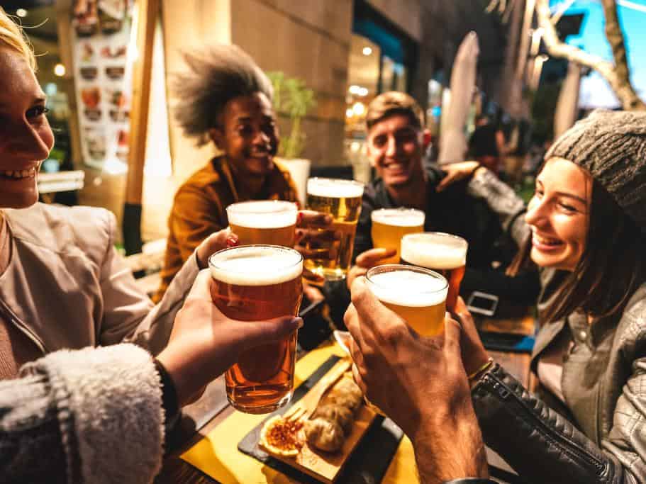 Group of people cheers-ing with full pints over food at a dinner table