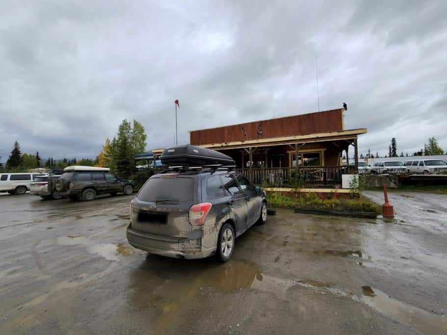 SUV in a muddy parking lot in front of a small wood building