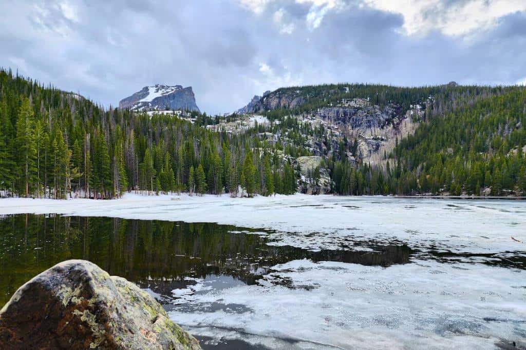 Partially frozen lake backed by trees and mountains