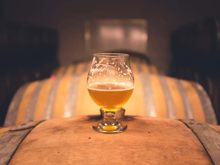 Half-full tulip glass sitting on top a wooden barrel