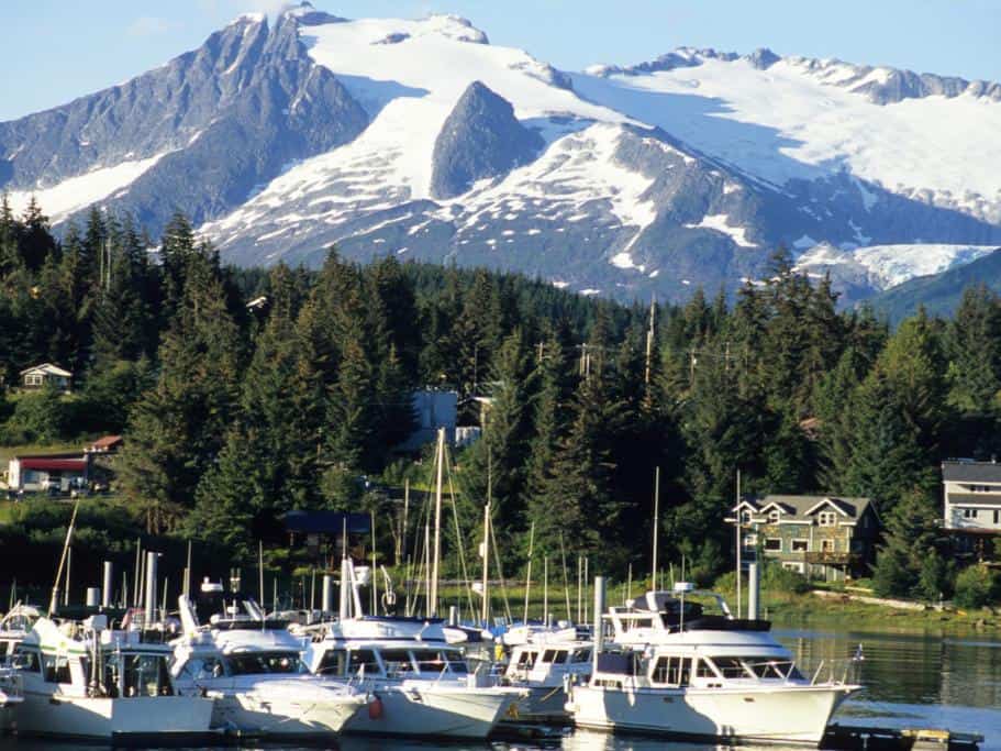 Small harbor situated in front of a small town that's backed by pine trees and mountains