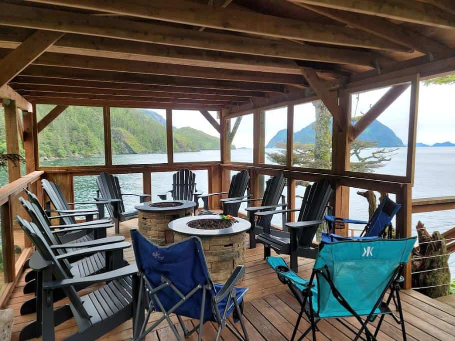 Group of adirondack chairs on a covered wooden deck overlooking the ocean and mountains