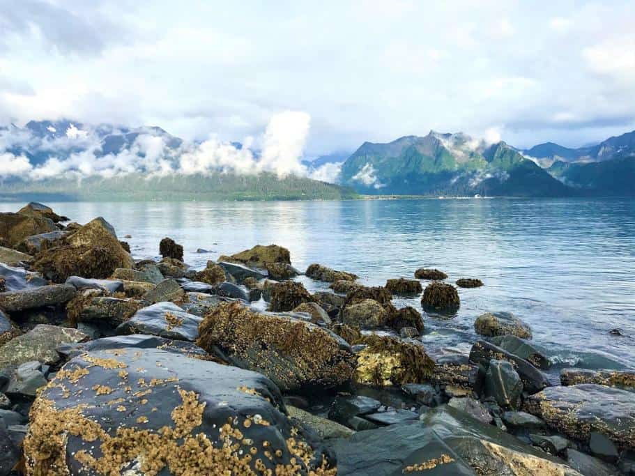Rocky oceanside against blue and green, cloud-covered mountains
