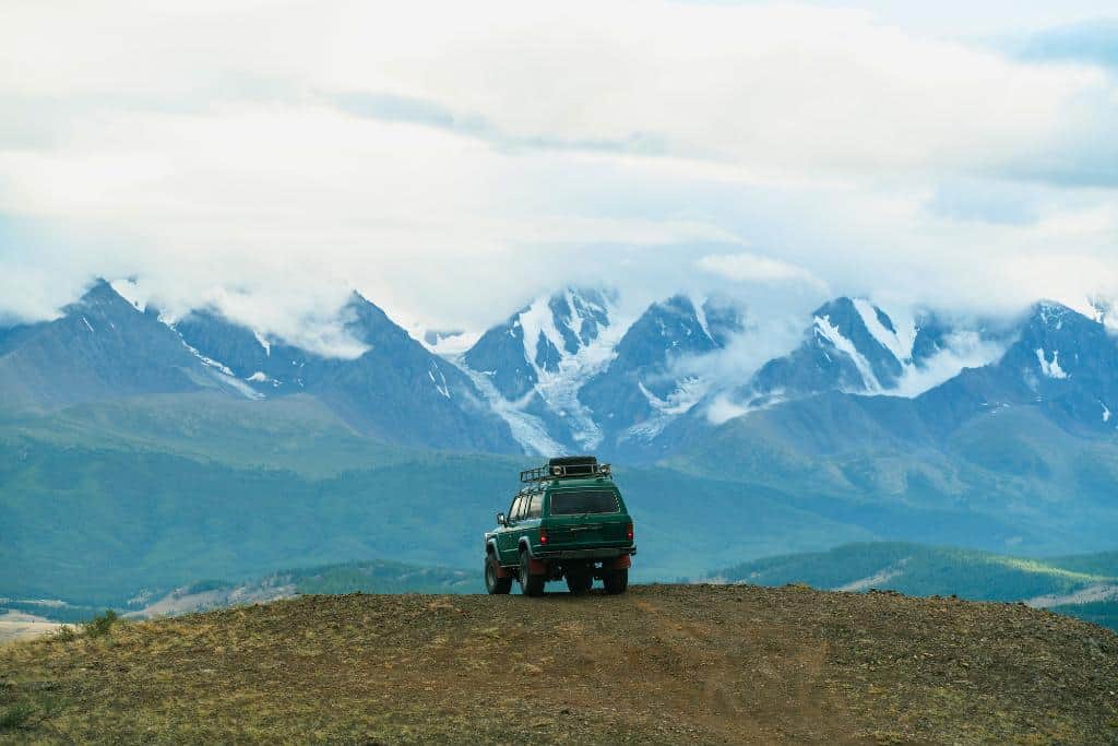 Large jeep with roof racks on a dirt overpass looking out at the mountains