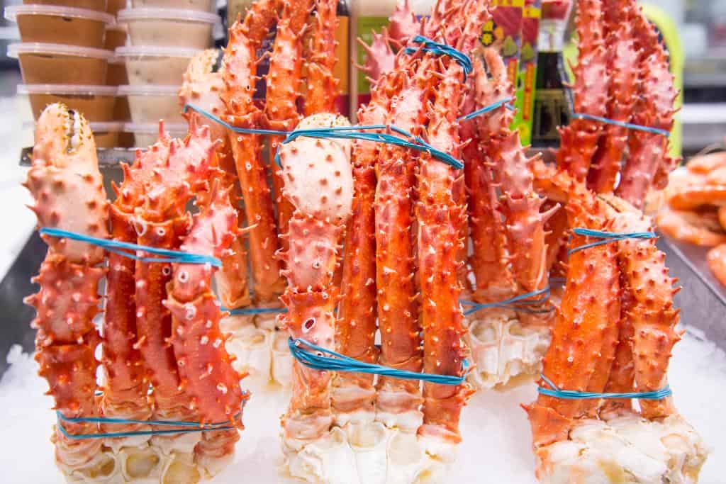 Groups of king crab legs wrapped in blue elastic bands sitting on ice