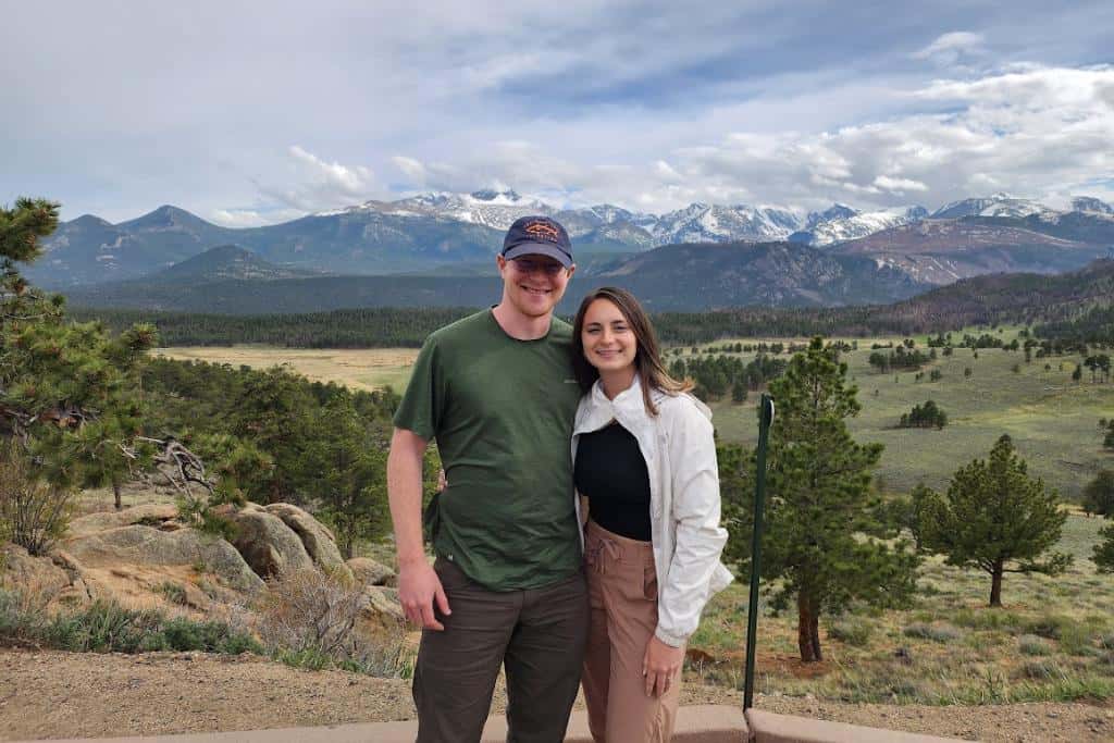 Man and woman smiling in front of a big valley and mountains