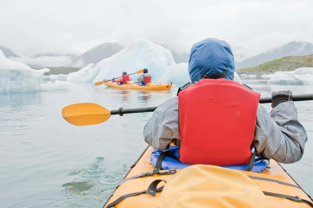 Two 2-seater, yellow kayaks with people in orange life vests paddling through large ice chunks