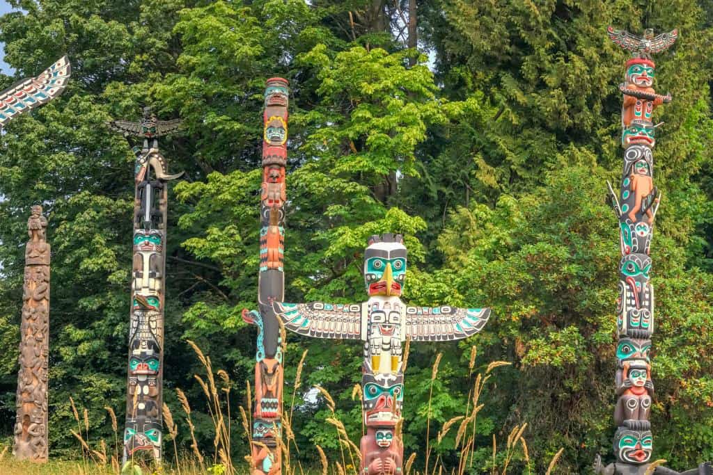 Collection of vibrantly-colored totem poles backed by tall trees