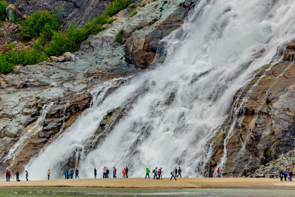Nugget Falls in Juneau, AK with many people walking on a sandy landing in front of it
