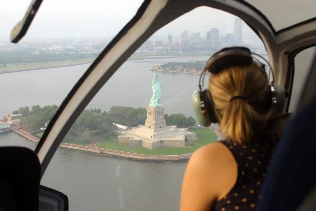 Girl with headset on in a helicopter flying over the Statue of Liberty