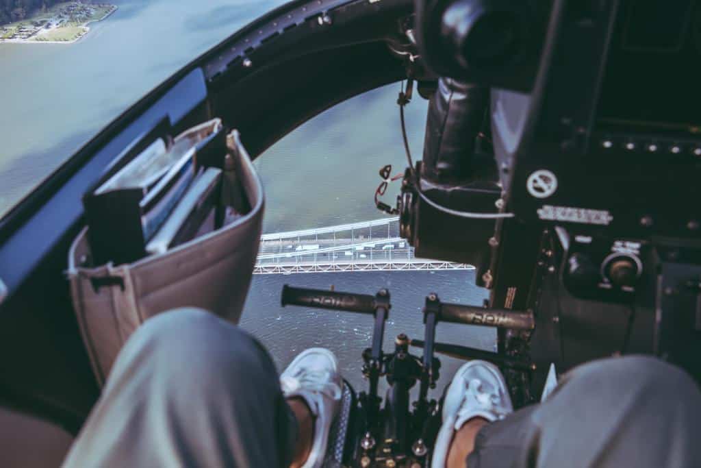 View of person's feet in a helicopter cockpit flying over a large bridge