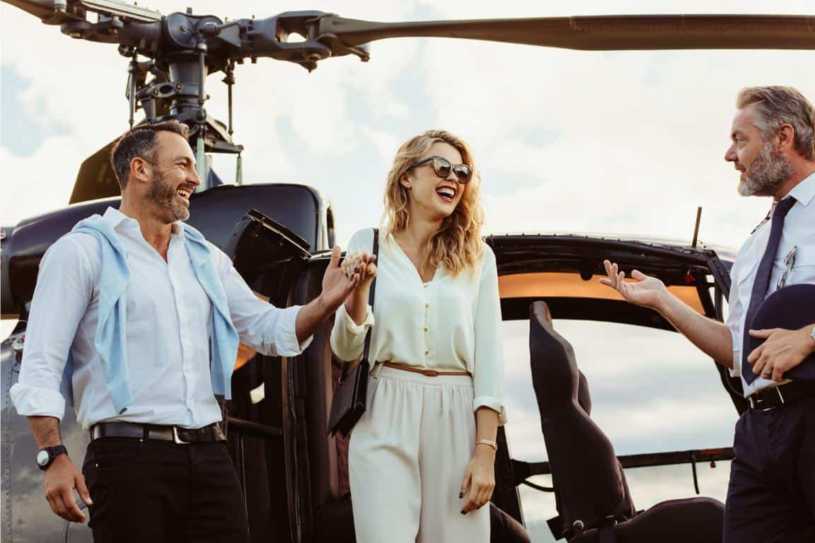 Two men and a woman smiling and walking out of a black helicopter