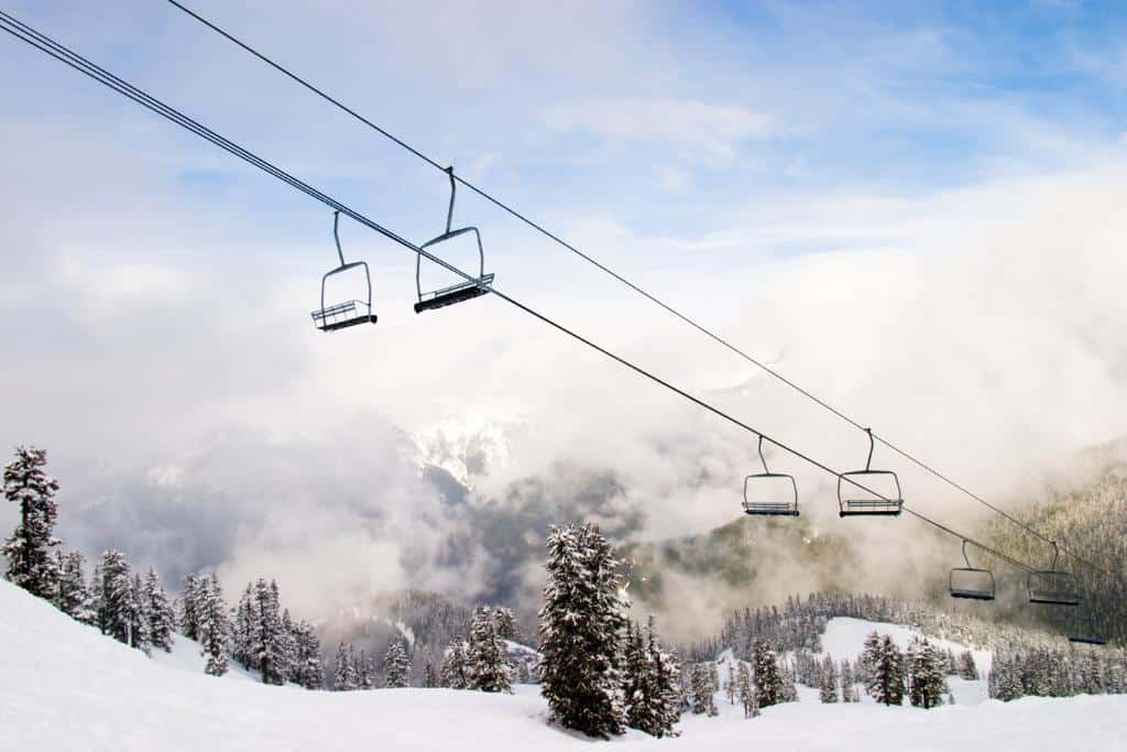 Empty ski lift chairs going over a very snowy landscape with trees and clouds