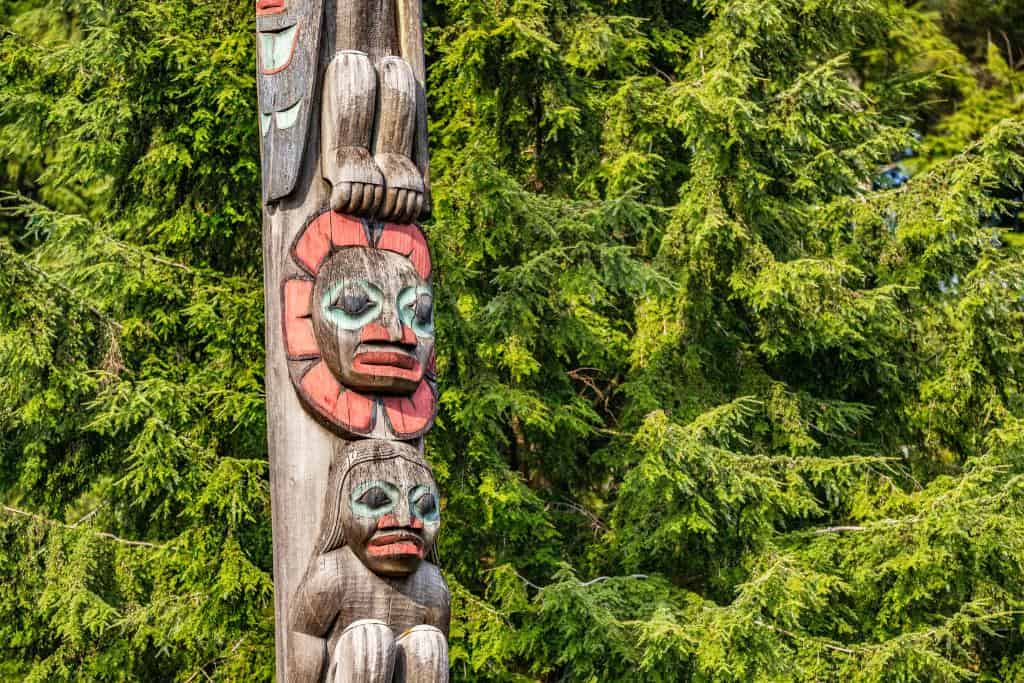 Close up of an Alaskan totem pole backed by pine trees