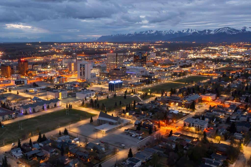 Nighttime aerial view of the city of Anchorage and the surrounding mountains under a thick layer of clouds
