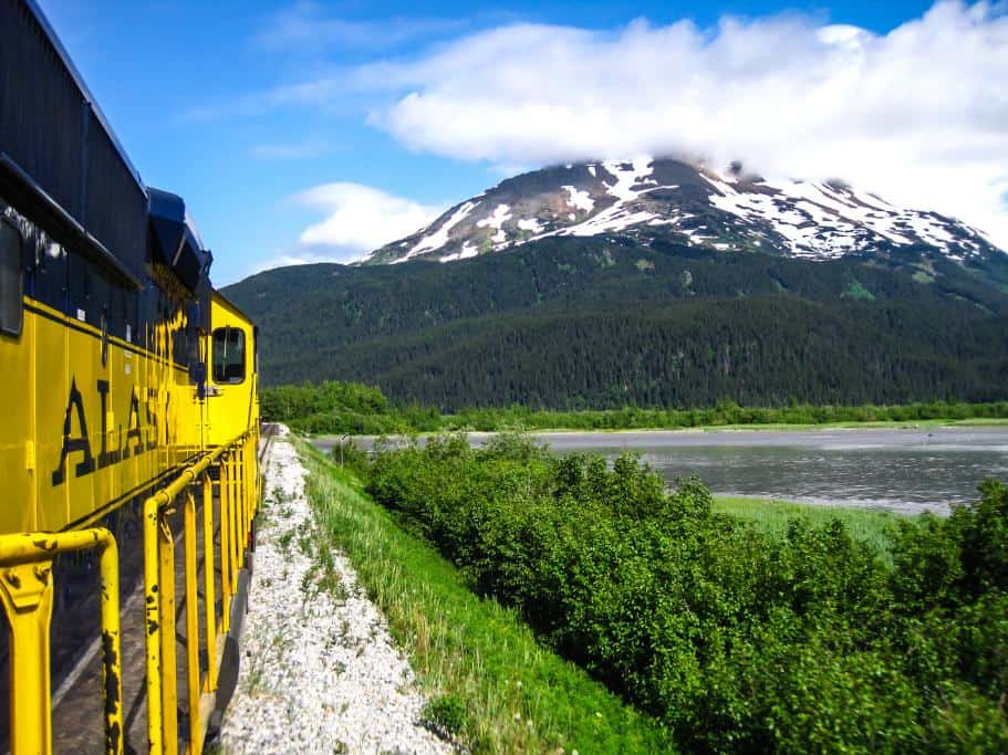 Yellow train riding along a green field and a distant mountain