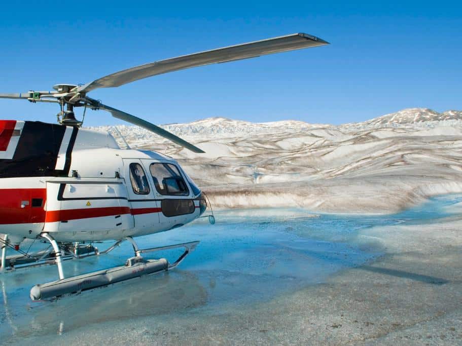 Red and white helicopter on a glacial body of water and white glacier