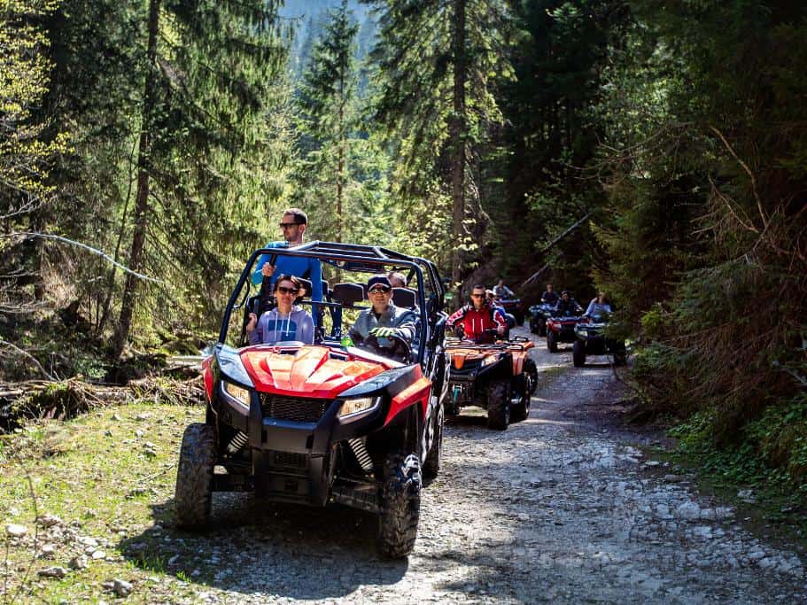 A line of ATVs riding through a trail in the woods on a sunny day