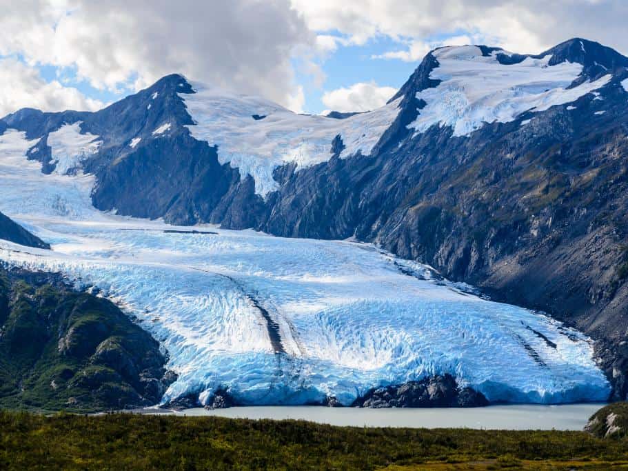 A bright blue glacier backed by giant mountains and smaller glaciers