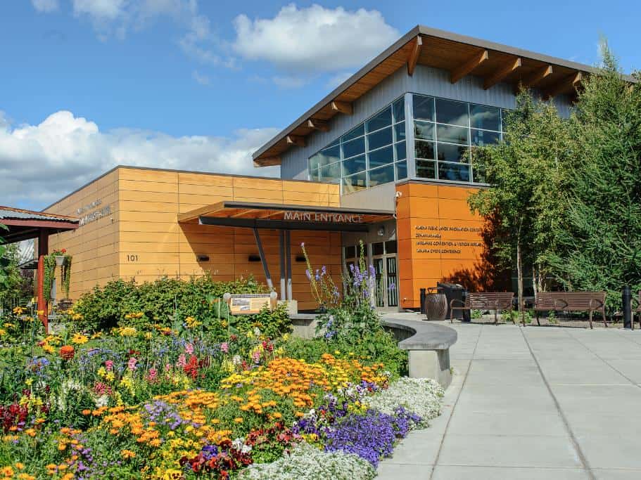 A flower garden, cement walkway, and square orange building with a "Main Entrance" sign