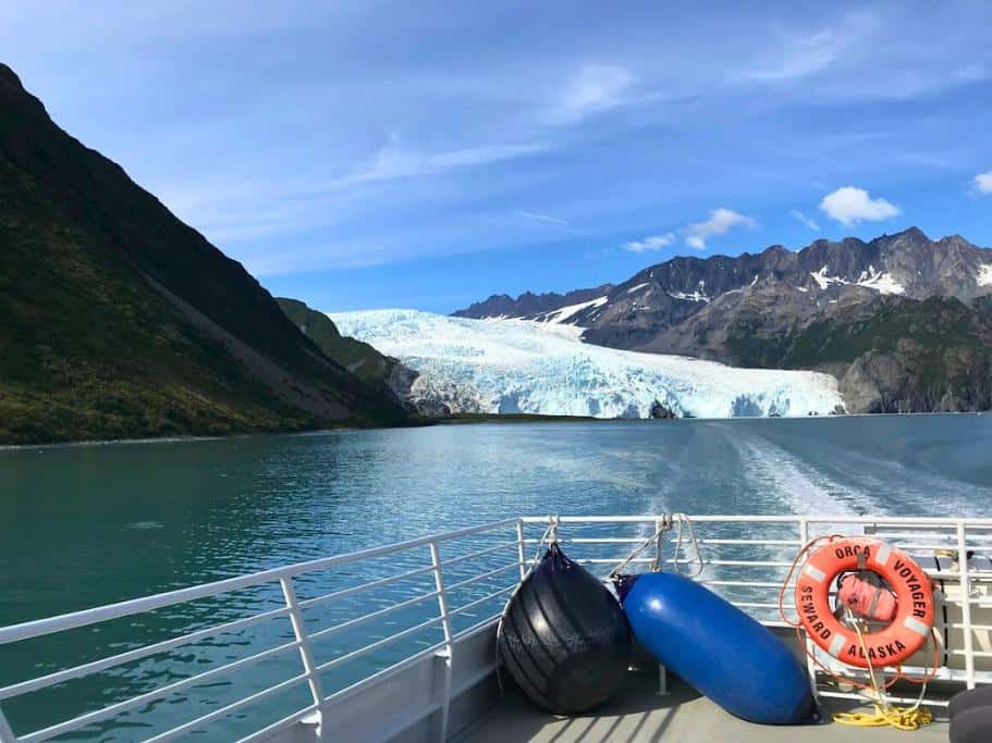 Back of a boat with black, blue, and orange buoys overlooking the ocean and a large glacier