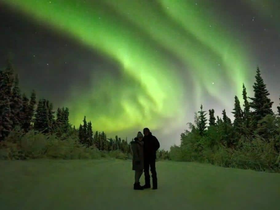 Green northern lights over the silhouette of a man and woman