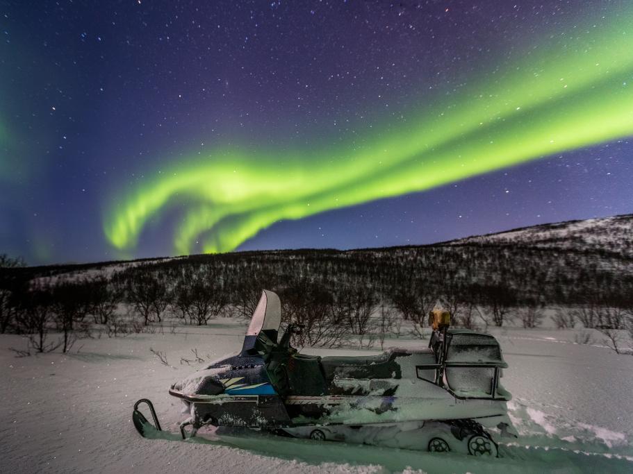 Snowmobile in a snowy field under the northern lights
