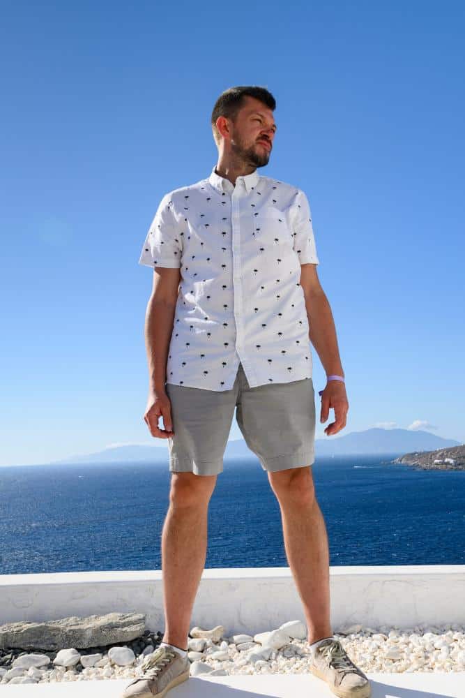Man in a white button-down shirt, gray shorts, and sneakers near the ocean