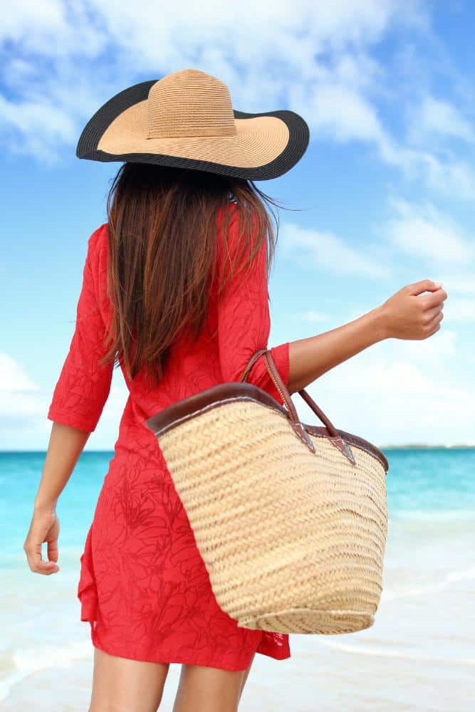 Gril with a straw hat and bag in a red dress on the beach